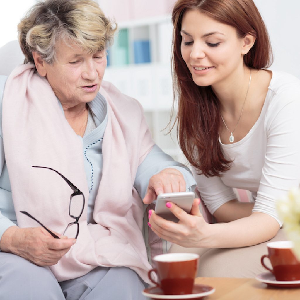 Smiling,Daughter,Showing,Smartphone,To,Senior,Woman,While,Drinking,Tea